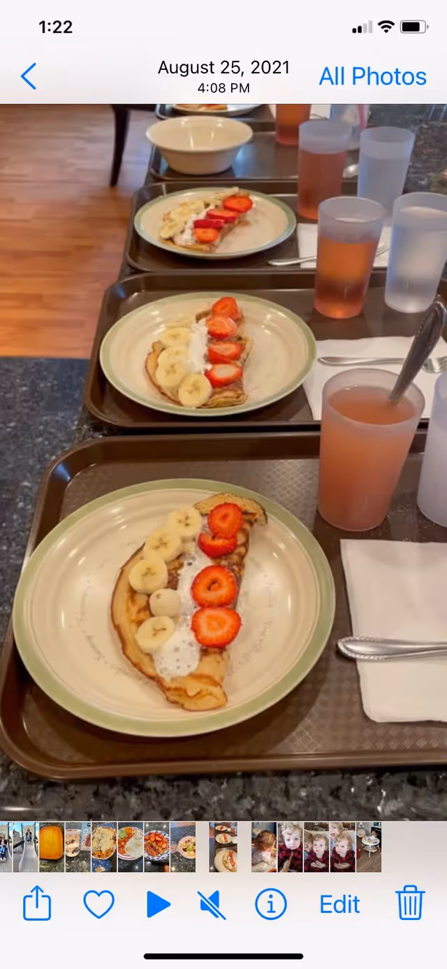 Three meal trays on a counter each with a plate of pancakes topped with banana and strawberry slices and cups of drink.