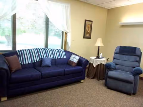 Blue sofa and recliner in a cozy senior living lounge by large windows.