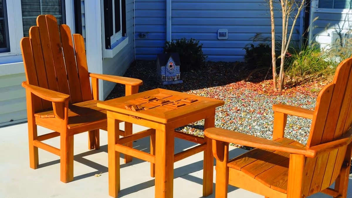 A wooden outdoor seating area featuring two Adirondack chairs and a small table, surrounded by decorative gravel and plants.