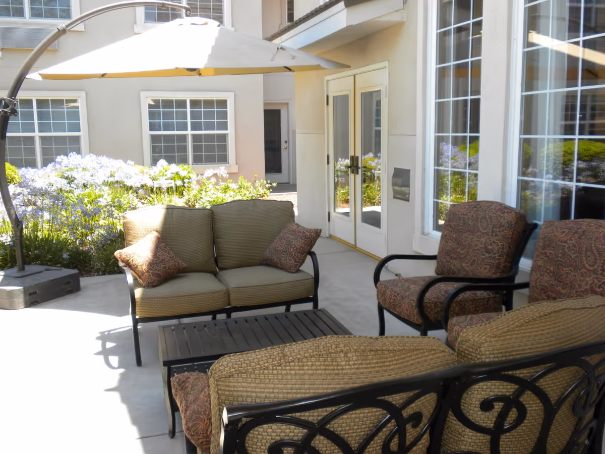 Outdoor patio seating area with cushioned sofa and chairs under a cantilever umbrella by building windows and doors.