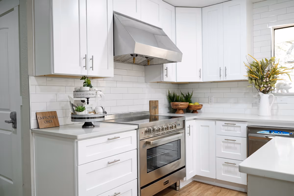 Bright modern white kitchen featuring a stainless steel stove and hood, white cabinetry, and countertop decor.