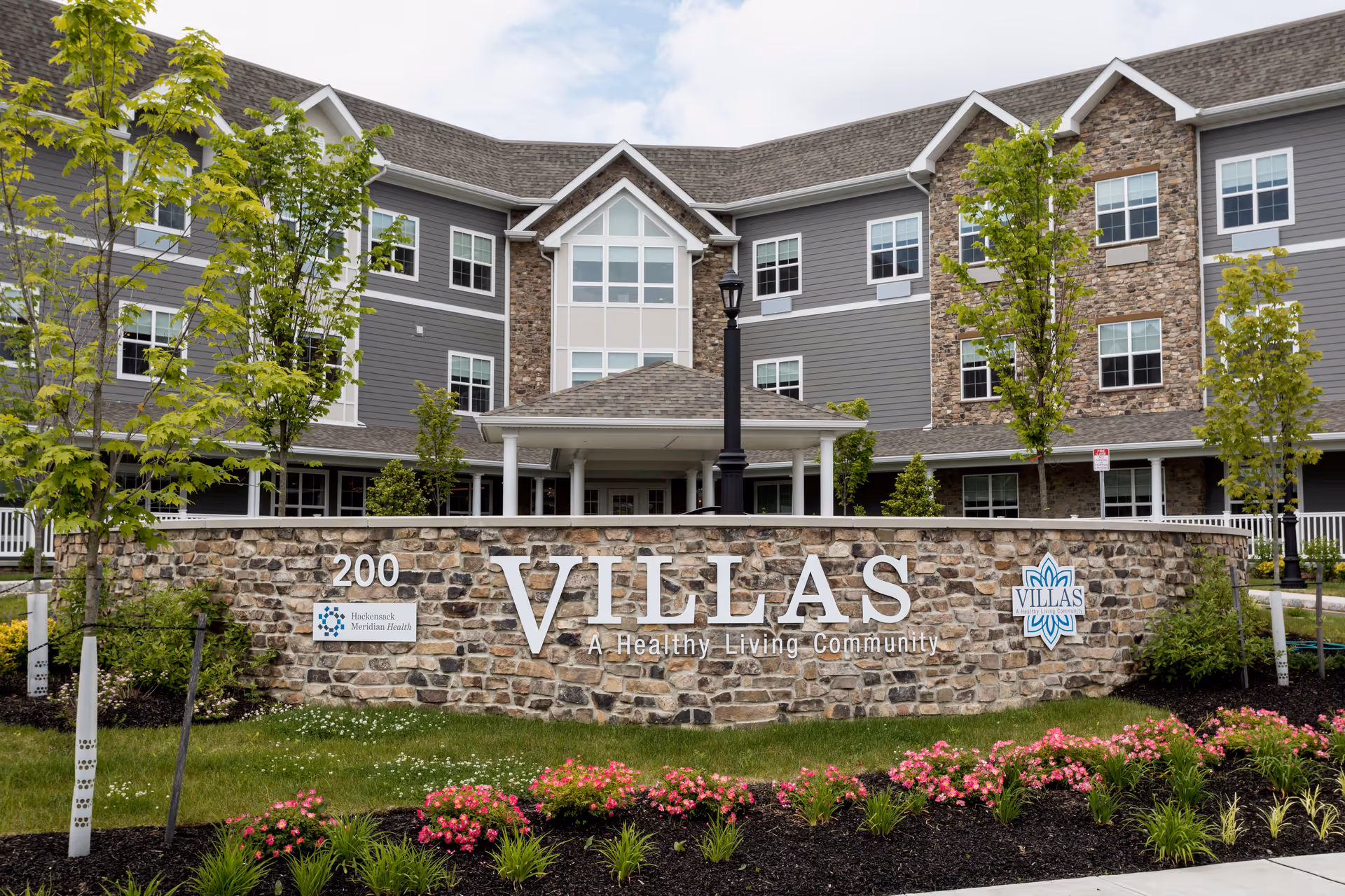 Stone sign reading 'VILLAS' in front of a three-story senior living building with landscaping.