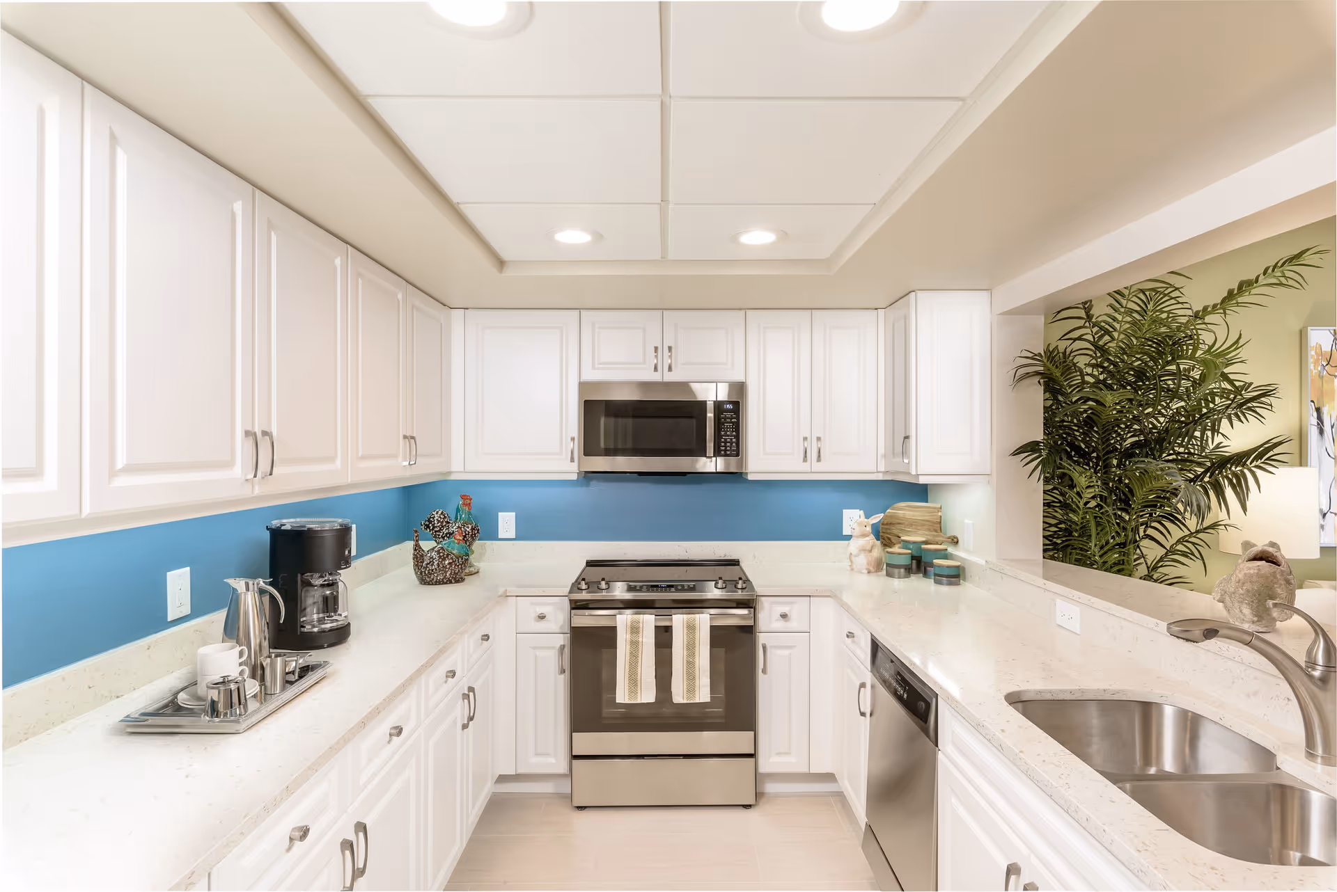 Bright modern kitchen with white cabinets, stainless steel appliances, a blue backsplash and a double sink on the counter.