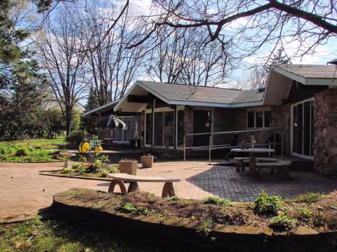 Exterior of Willow Haven CBRF with brick patio, benches, and surrounding trees.
