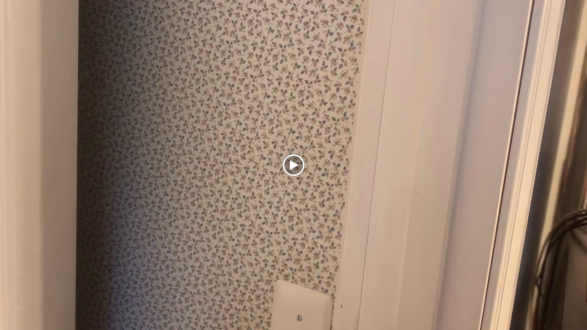 A small interior space with floral patterned wallpaper on one wall and white painted door frames and walls surrounding it.