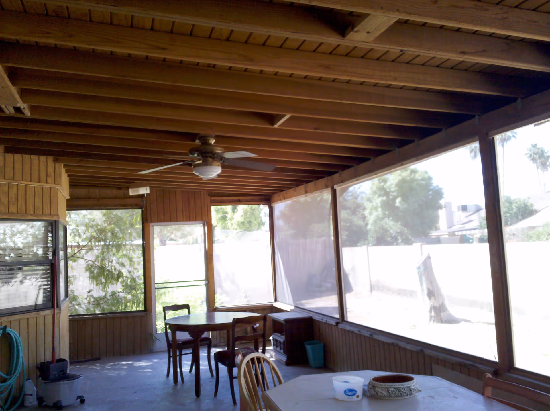 Wood-paneled screened-in porch with exposed beam ceiling, ceiling fan, and a table with chairs overlooking the yard.