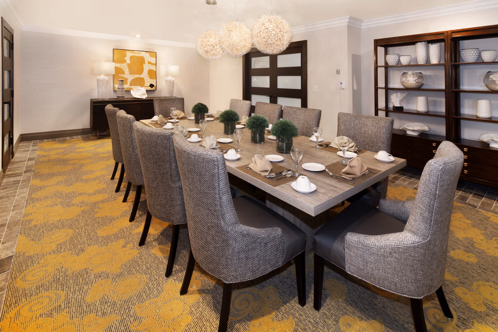 Large dining room with a long wood table set for a meal, upholstered chairs, pendant lights, and decorative shelving.
