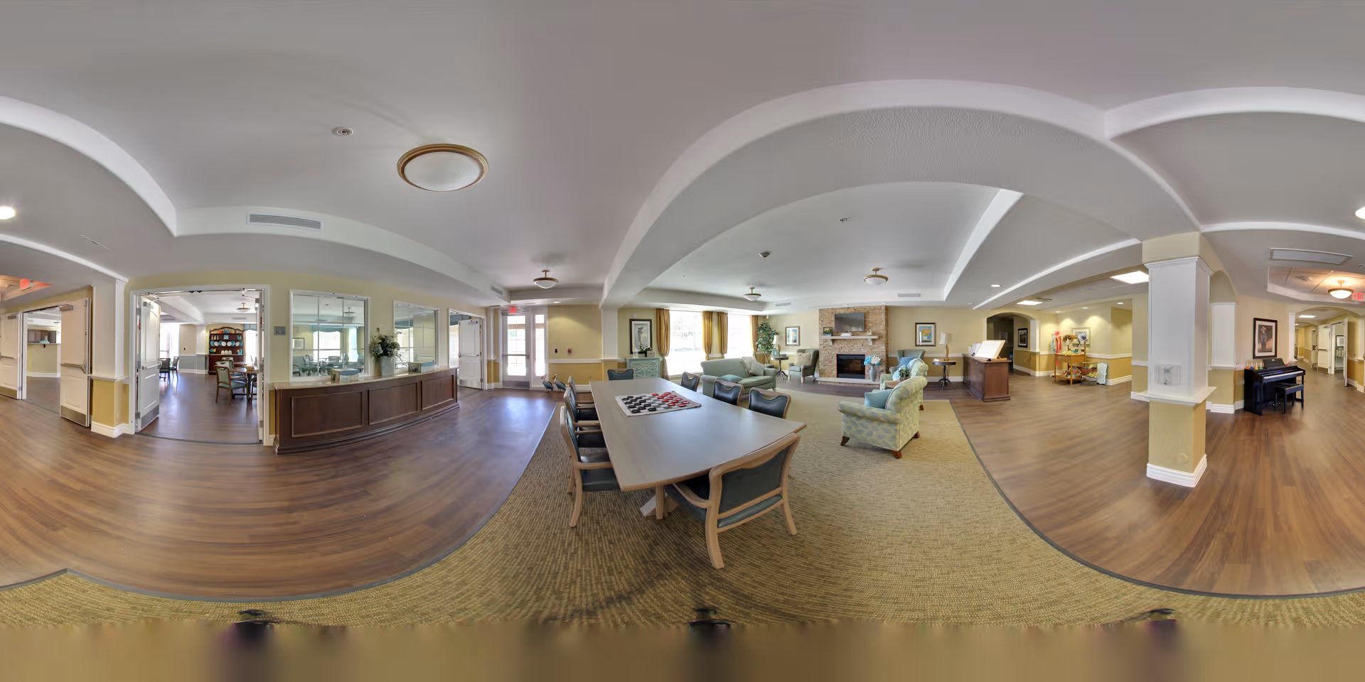 Spacious communal living area with a long table, seating clusters, a fireplace, and a reception desk.