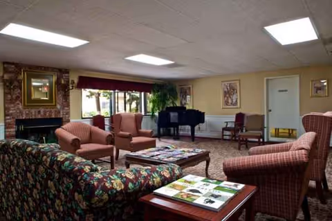 A spacious senior living lounge with sofas, chairs, coffee tables, and a grand piano.