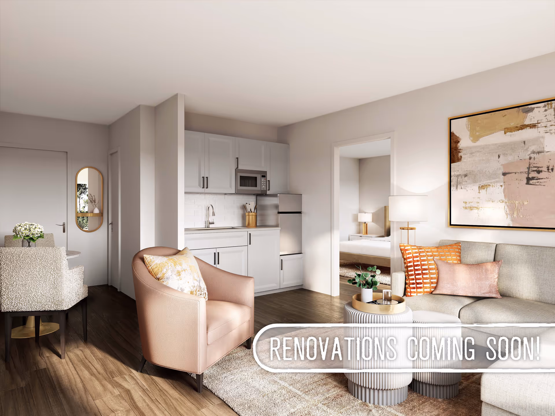 A modern living space featuring a small kitchen with white cabinets, a stainless steel refrigerator and microwave, a cozy seating area with a beige sofa adorned with orange and pink pillows, a round coffee table with a plant and glass, a pink armchair with a decorative pillow, and a dining area with a table and chairs. A doorway leads to a bedroom with a bed and lamp. The room has wooden flooring and neutral-colored walls with a large abstract painting. Text overlay reads 'RENOVATIONS COMING SOON!'