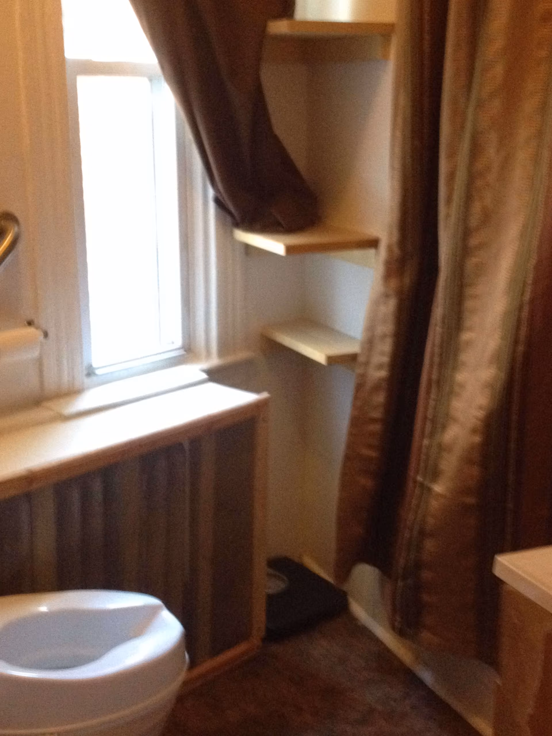 Small bathroom with a toilet, a window, corner shelves, and a brown shower curtain.