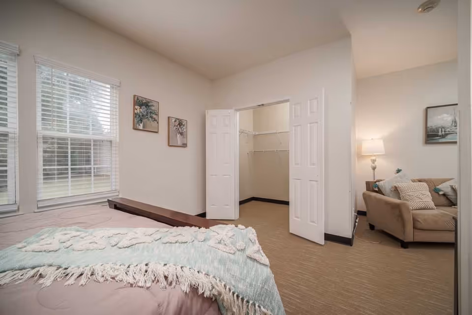 Well-lit bedroom with a bed, an open walk-in closet, and a sitting area with a couch and lamp.