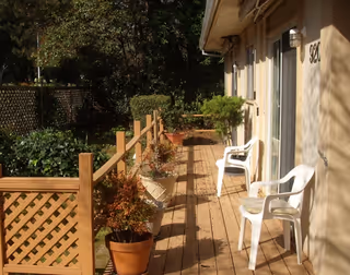 Wooden outdoor deck with white plastic chairs and potted plants along a beige building.