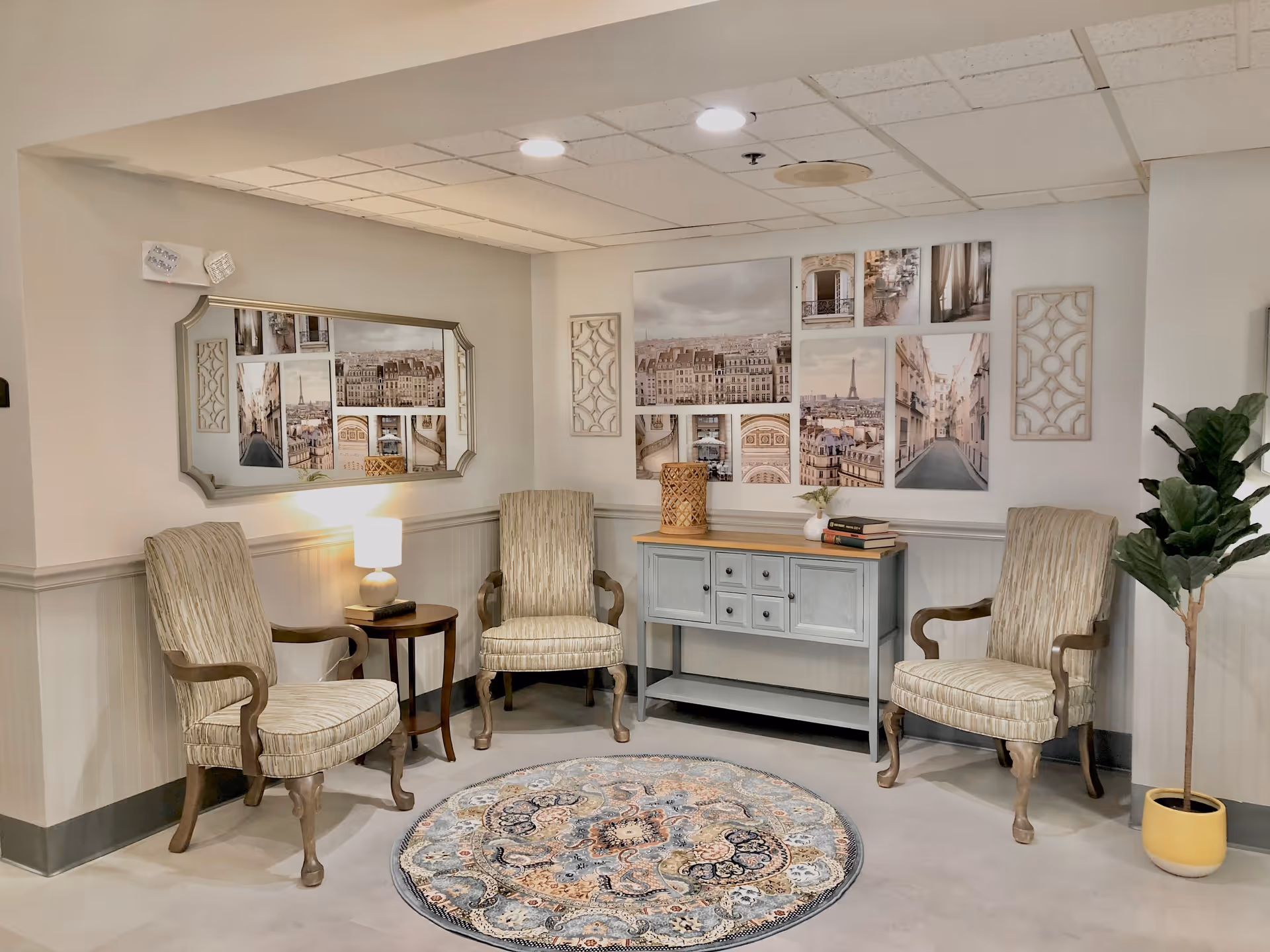 Small sitting area with three upholstered armchairs around a round patterned rug, a console table with decor and framed wall art.