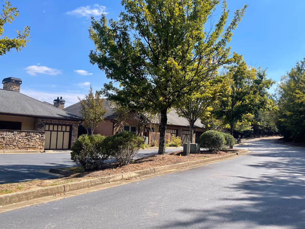 Front exterior of TerraBella Sugarloaf showing building garages and a tree-lined driveway under a blue sky.