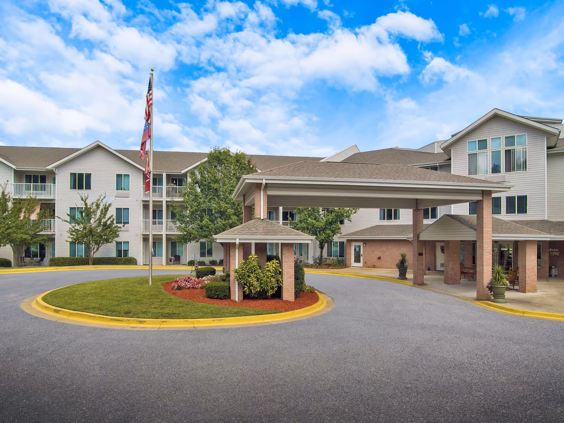 Exterior view of TerraBella Riverplace with a covered driveway, flag, and landscaped entrance.