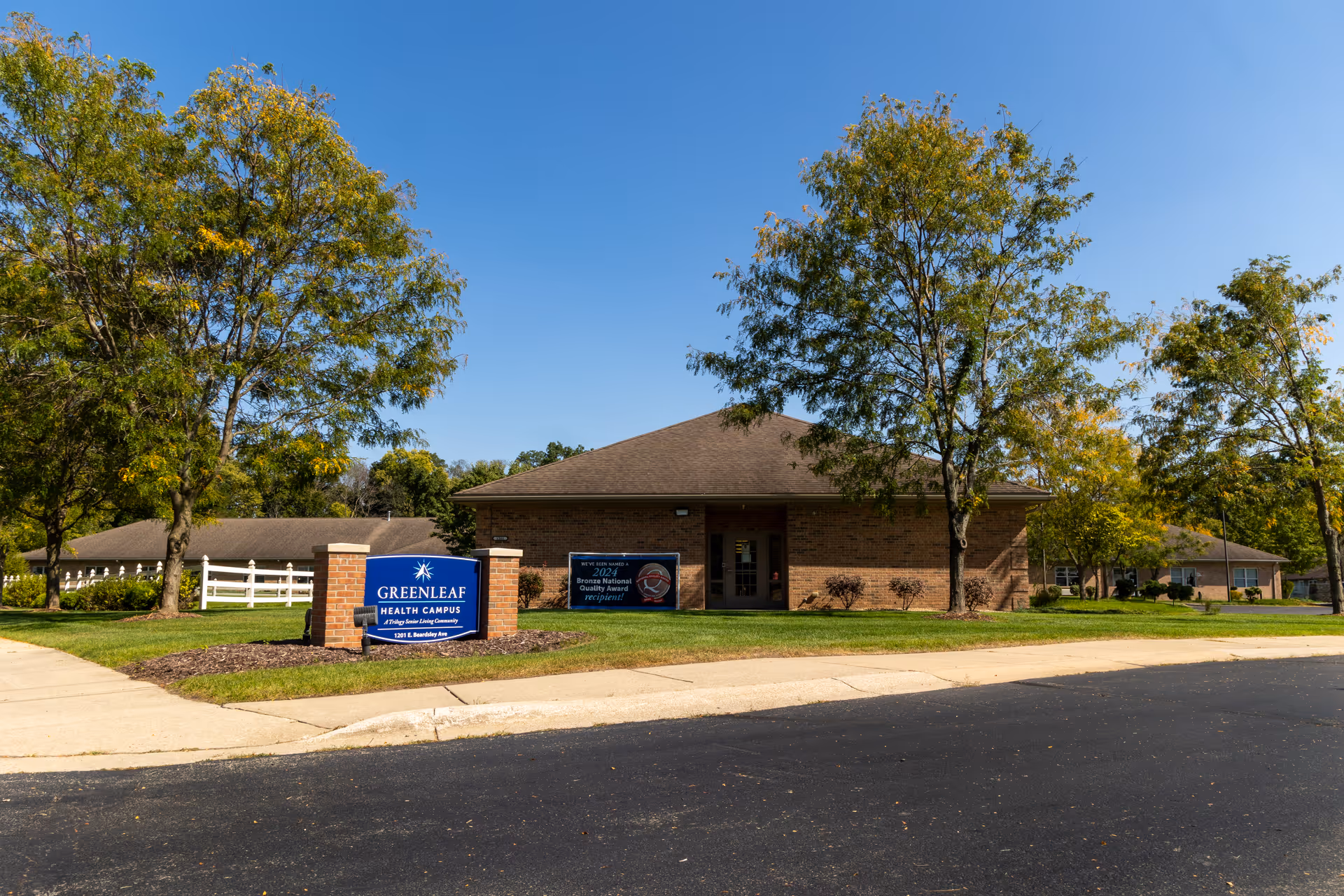 Brick single-story Greenleaf Health Campus building with lawn, trees, and a blue entrance sign.