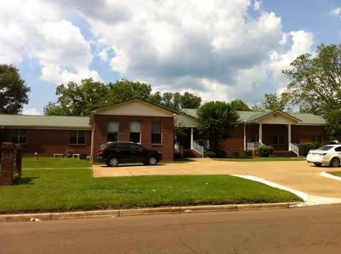 Front exterior of a single-story brick senior care facility with parked cars.