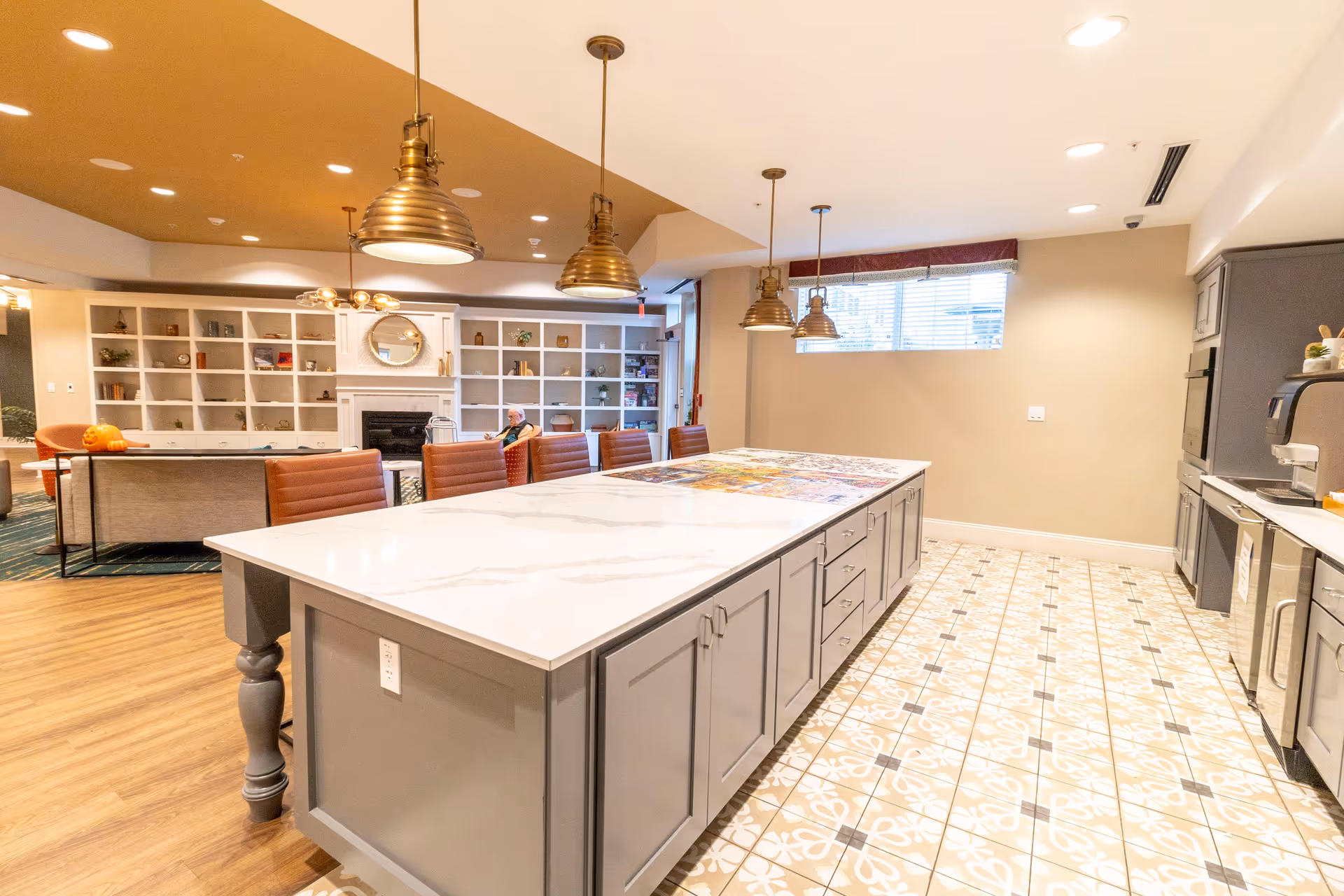 Bright communal kitchen and lounge area with a large central island, pendant lights, and built-in shelving and seating.