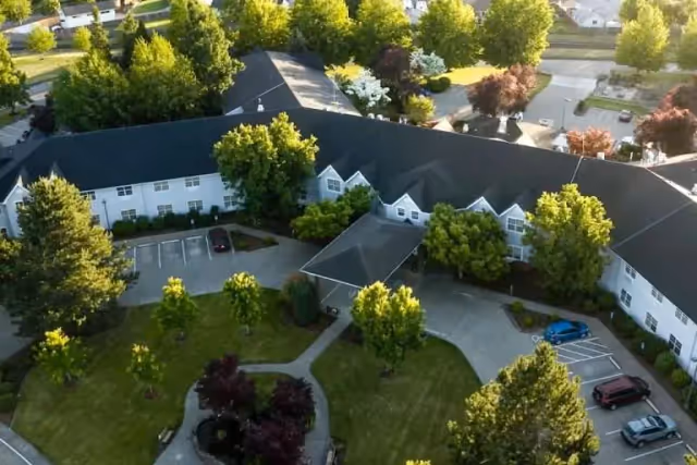 Aerial view of a large, U-shaped senior living campus with parking lots, driveways, and trees.