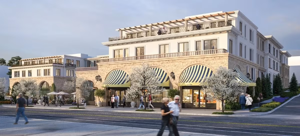 Front exterior of a multi-story senior living building with striped awnings, landscaping, and people walking on the sidewalk.