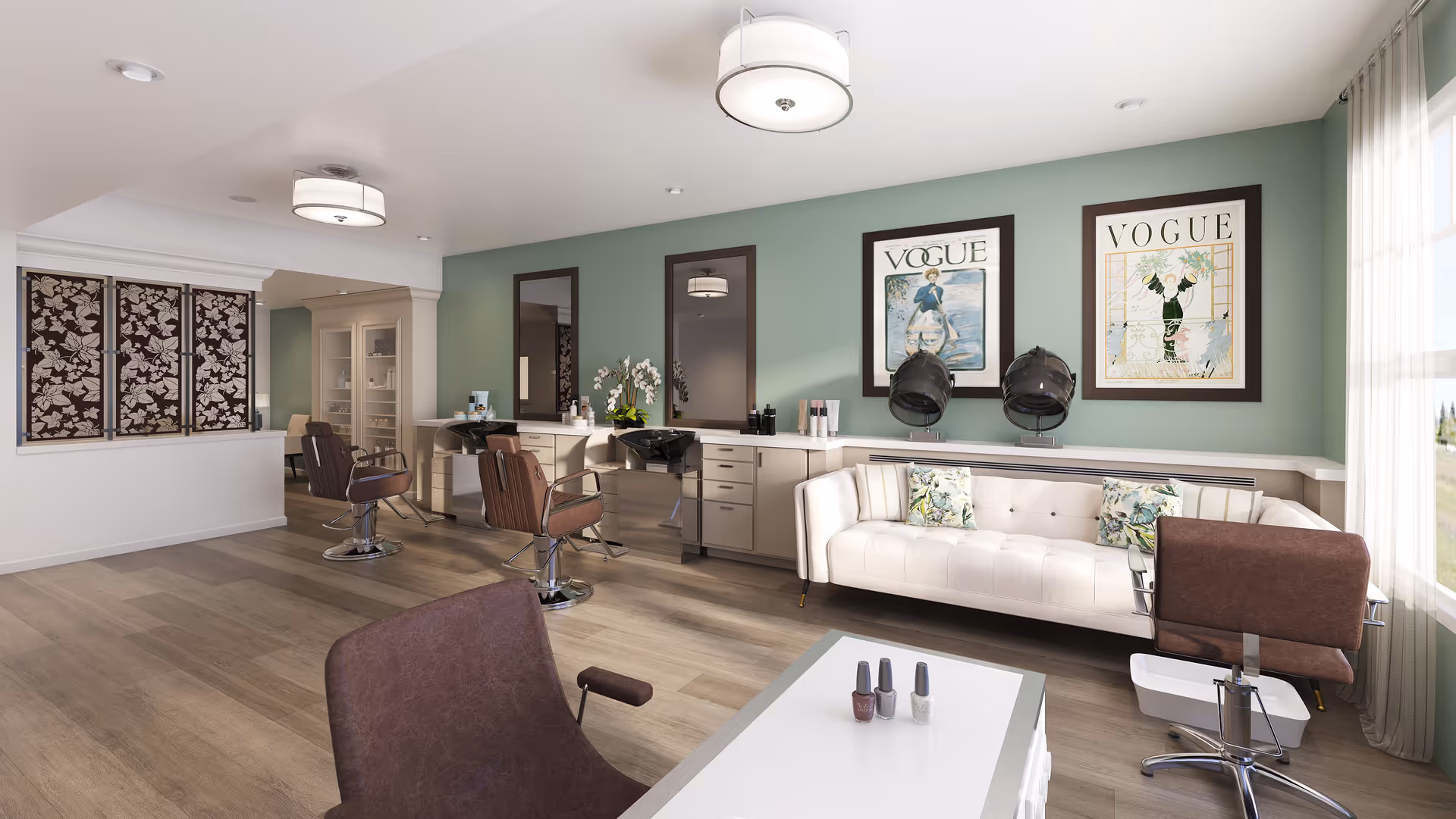 A bright and modern salon area with two brown salon chairs in front of mirrors and hair washing sinks, a white tufted sofa with floral pillows, two vintage Vogue magazine covers framed on a green wall, and a small table with three bottles of nail polish. The room has wood flooring, large windows with sheer curtains, and decorative ceiling lights.