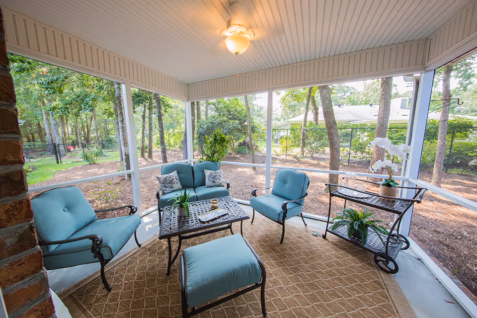 Screened-in porch with teal cushioned patio furniture, a coffee table and rolling side table overlooking a wooded yard.