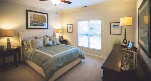 Well-lit bedroom with a bed, nightstands, lamps, a dresser, and a window with blinds.