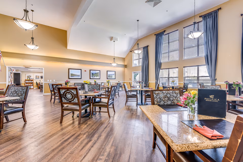 Bright, spacious senior dining room with multiple set tables, high ceilings, large windows and pendant lights.