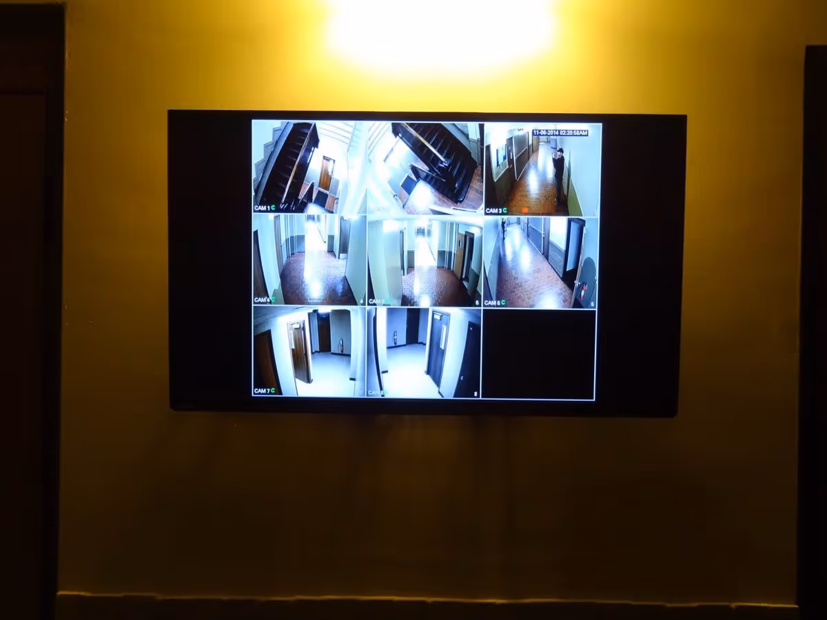 A wall-mounted monitor displaying multiple security camera feeds showing various indoor hallways and staircases within a building.