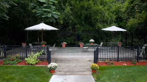 Wooden outdoor patio with umbrellas, seating, and potted plants beside a green lawn.