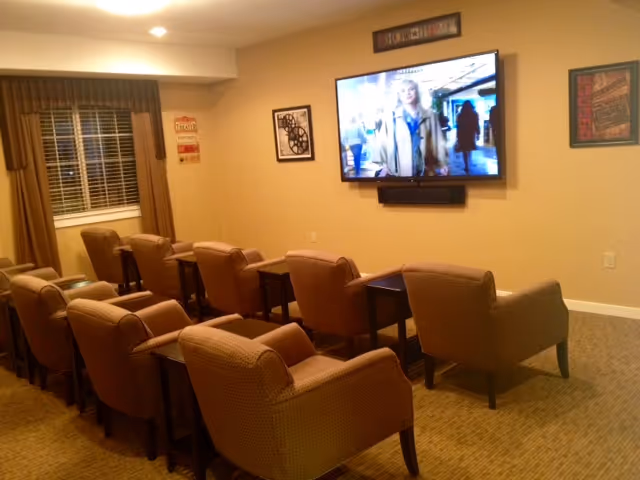 Small community media room with rows of upholstered armchairs facing a wall-mounted flat-screen TV.