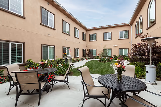 Enclosed two-story courtyard with round metal patio tables and chairs, flowerbeds and a small grassy area.