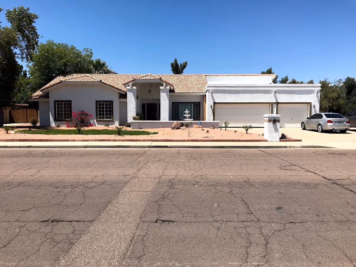 Front exterior of a single-story white stucco house with a tiled roof, three-car garage, driveway, and desert landscaping.