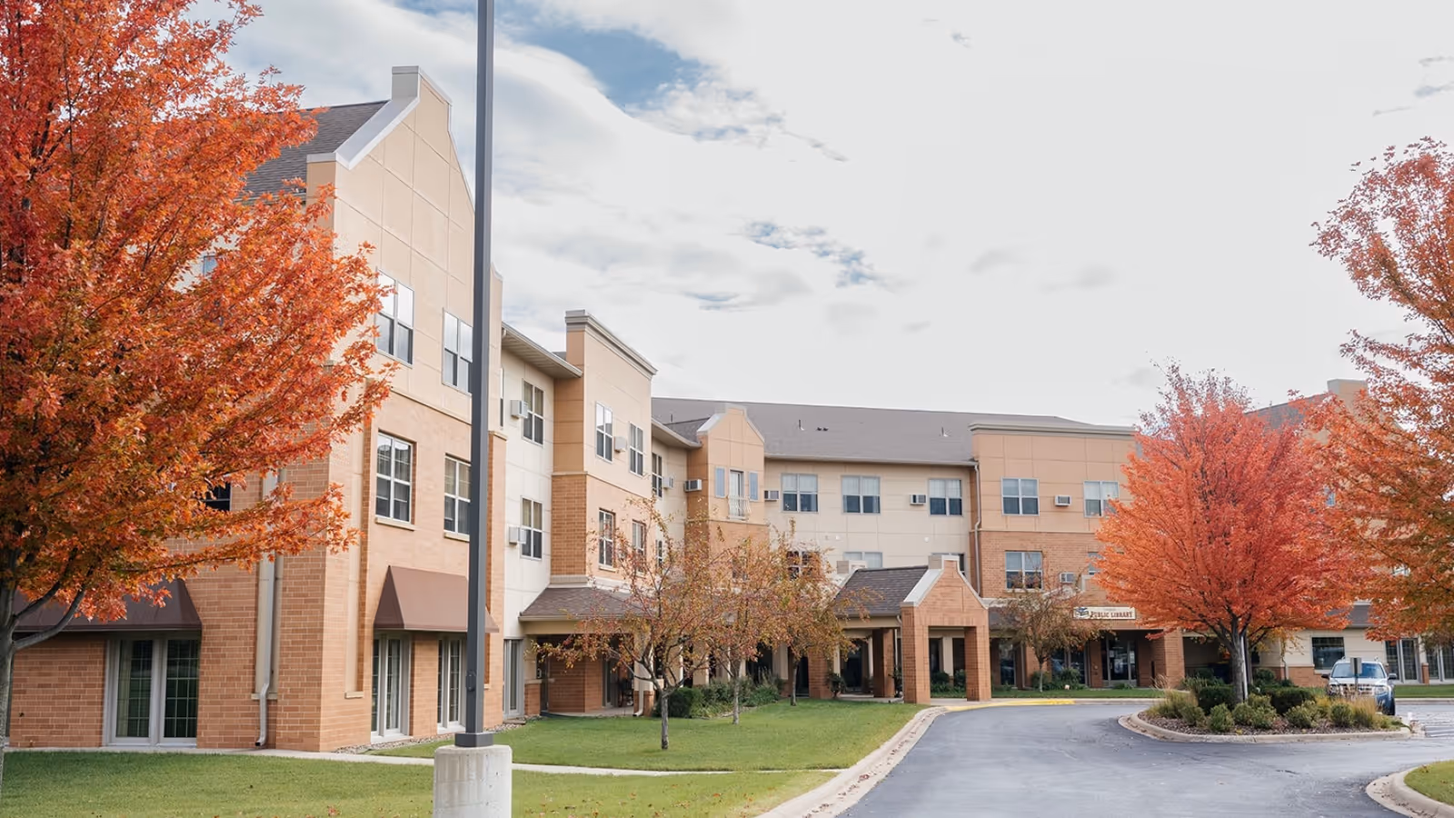 Exterior front view of a three-story senior living building with fall-colored trees and a curved driveway.