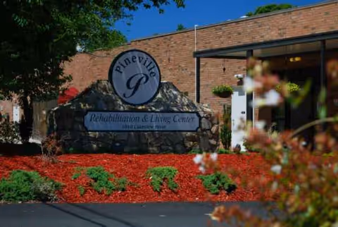 Entrance sign for Pineville Rehabilitation & Living Center with red landscaping.