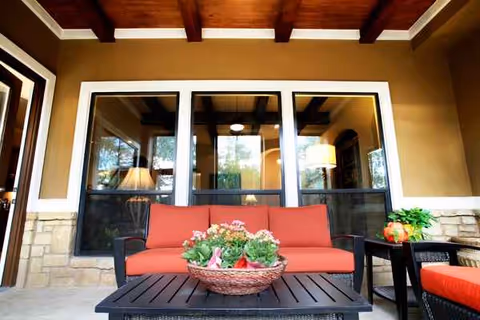 Outdoor covered patio with red-cushioned sofa, coffee table, lanterns, and potted plants.