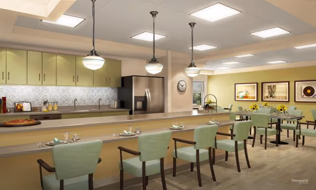 Communal dining and kitchen area with a long counter, green upholstered chairs, pendant lights, and tables in a bright interior.