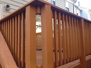 Close-up view of a wooden deck railing attached to a residential building with beige siding and multiple windows.