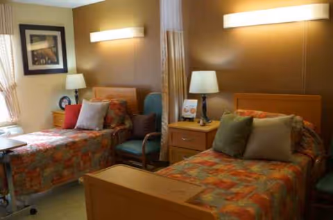 Two twin beds with colorful quilts in a shared senior living resident bedroom.