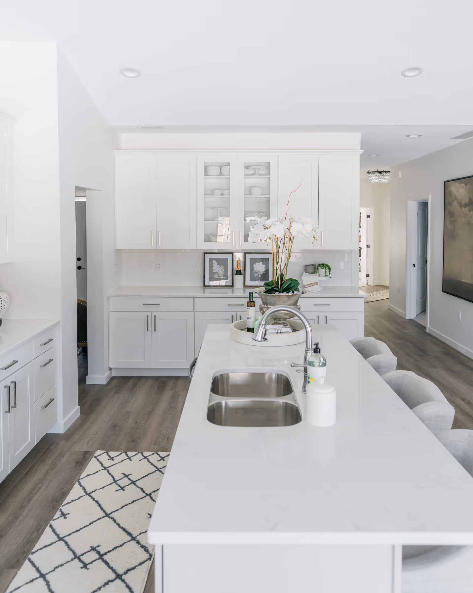 Bright modern white kitchen with a long island and sink, bar stools, and white cabinets.