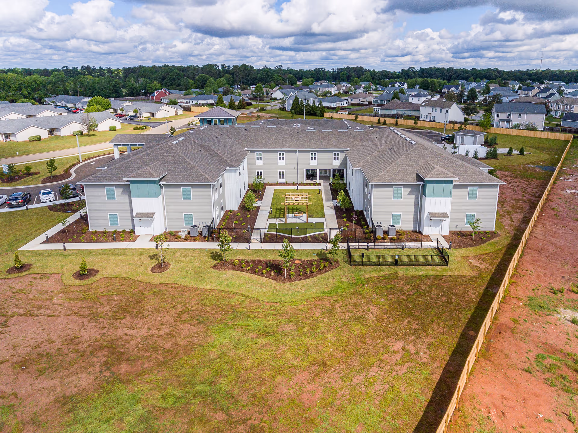 Aerial view of a U-shaped senior living building surrounding a landscaped central courtyard, with lawns and nearby houses.