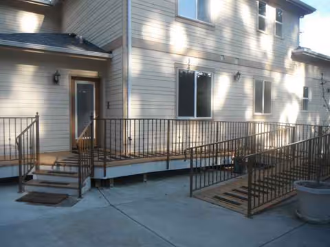 Exterior view of a two-story beige building with a metal ramp and wooden deck.