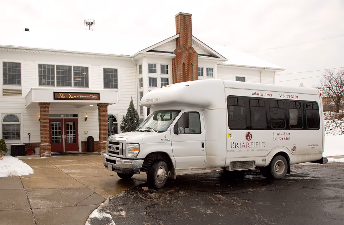 Exterior view of The Inn at Christine Valley building with a white Briarfield shuttle bus parked in front on a snowy day.