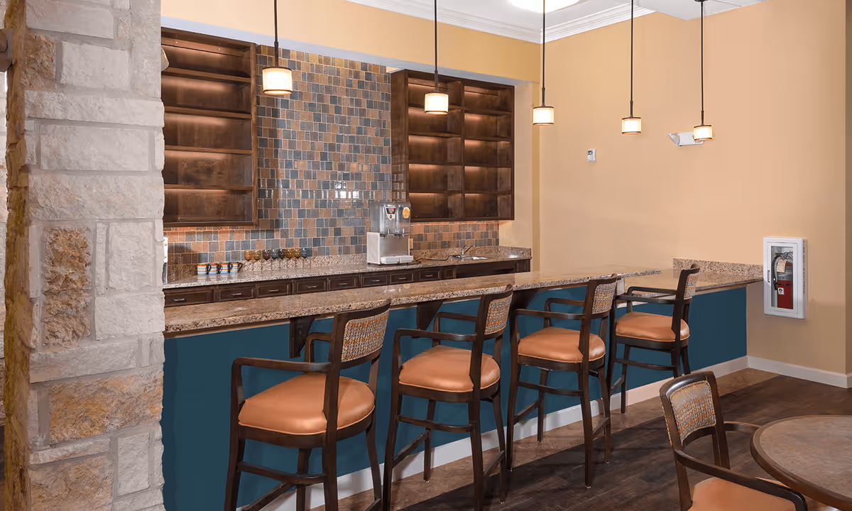 Bar-style dining counter with four high chairs, pendant lights, a tiled backsplash and open shelving in a communal dining area.