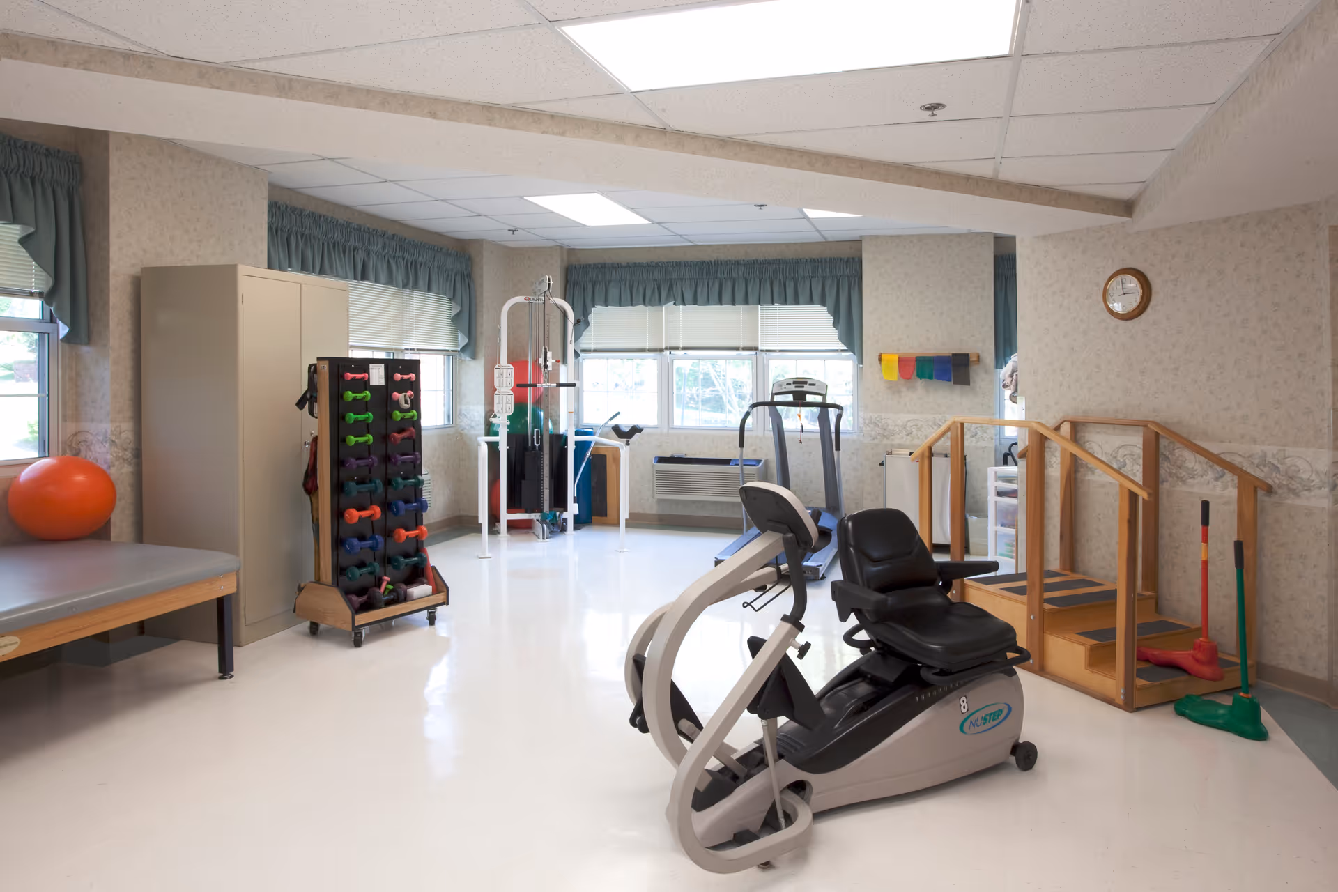 Bright rehabilitation/exercise room with a recumbent bike, treadmill, free weights, therapy stairs and other exercise equipment.