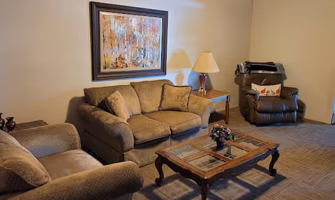 Living room featuring a sofa and loveseat, recliner, wooden coffee table, side table with lamp, and framed wall art.