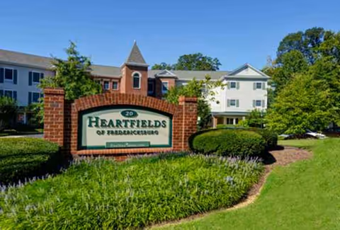 Exterior view of a senior living building with a brick sign and landscaping.