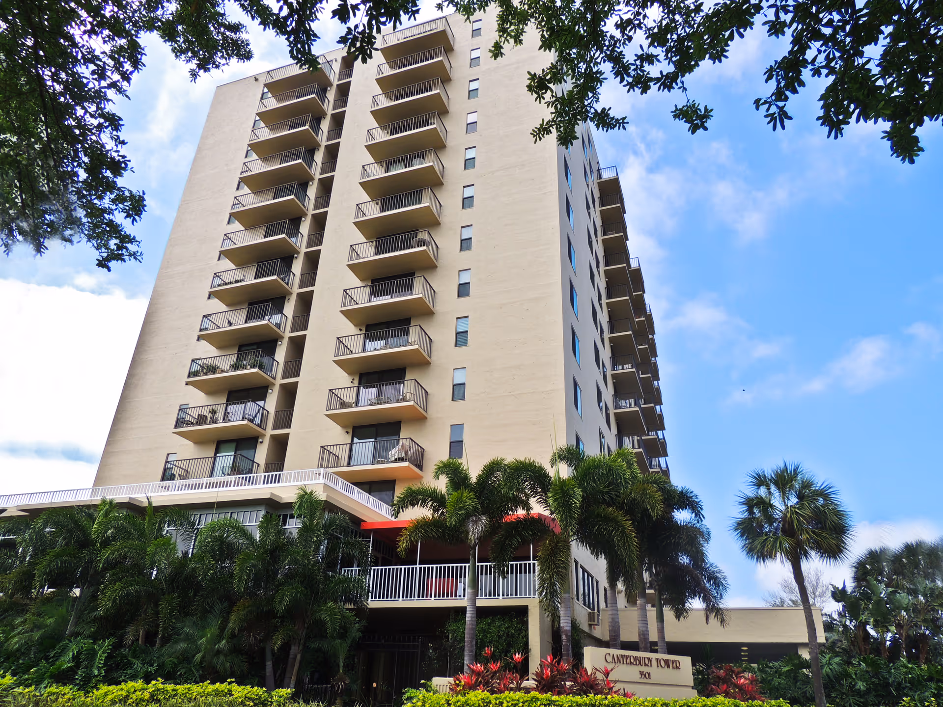 Tall beige residential building with multiple balconies, palm trees, and an entrance sign reading Canterbury Tower.
