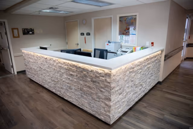 Stone-faced reception/nurse station in a hallway with office chairs, equipment, and doors behind it.